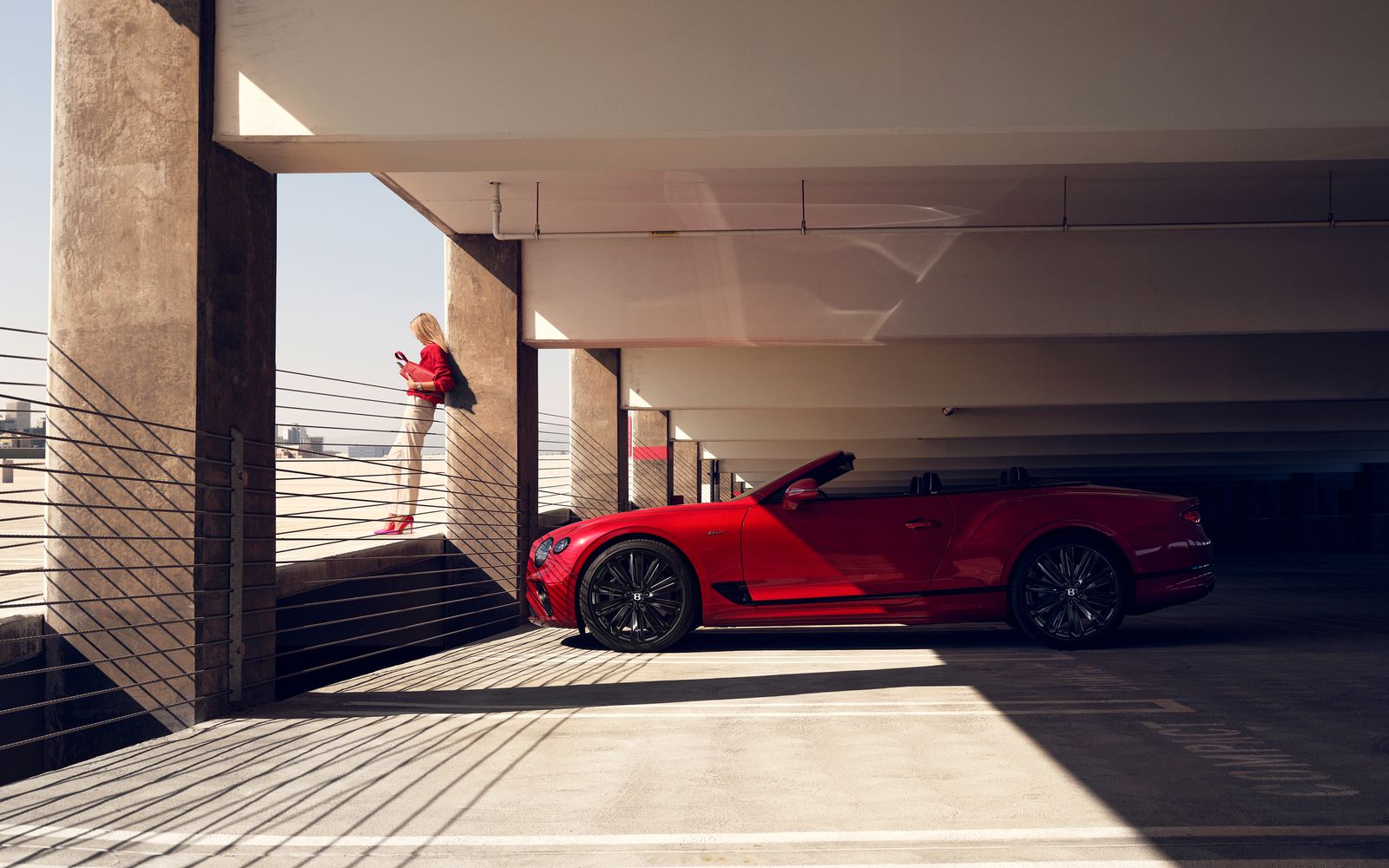 Red Bentley convertible beneath concrete architecture, a woman in red on the stairs