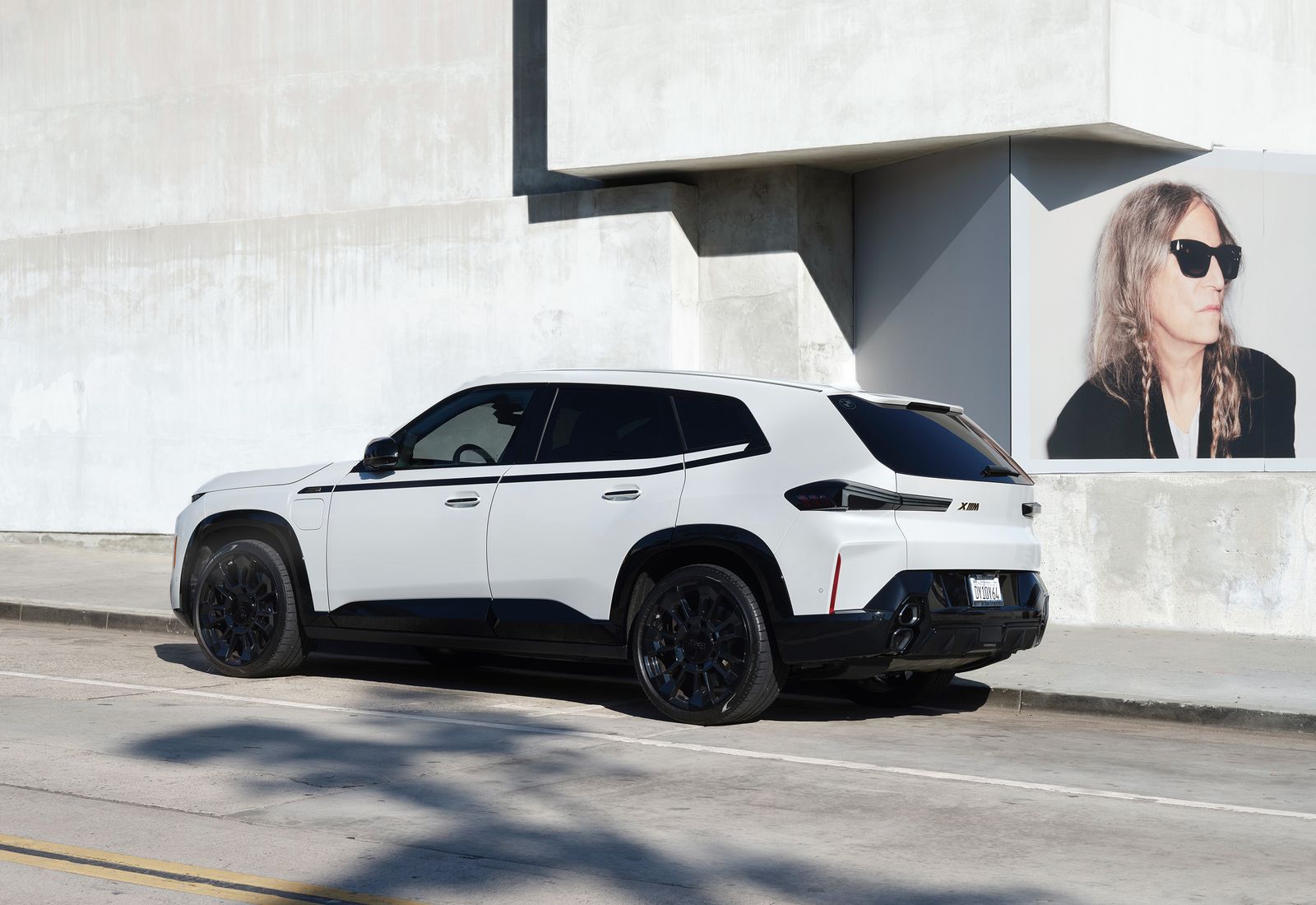 White BMW XM against concrete and a large portrait