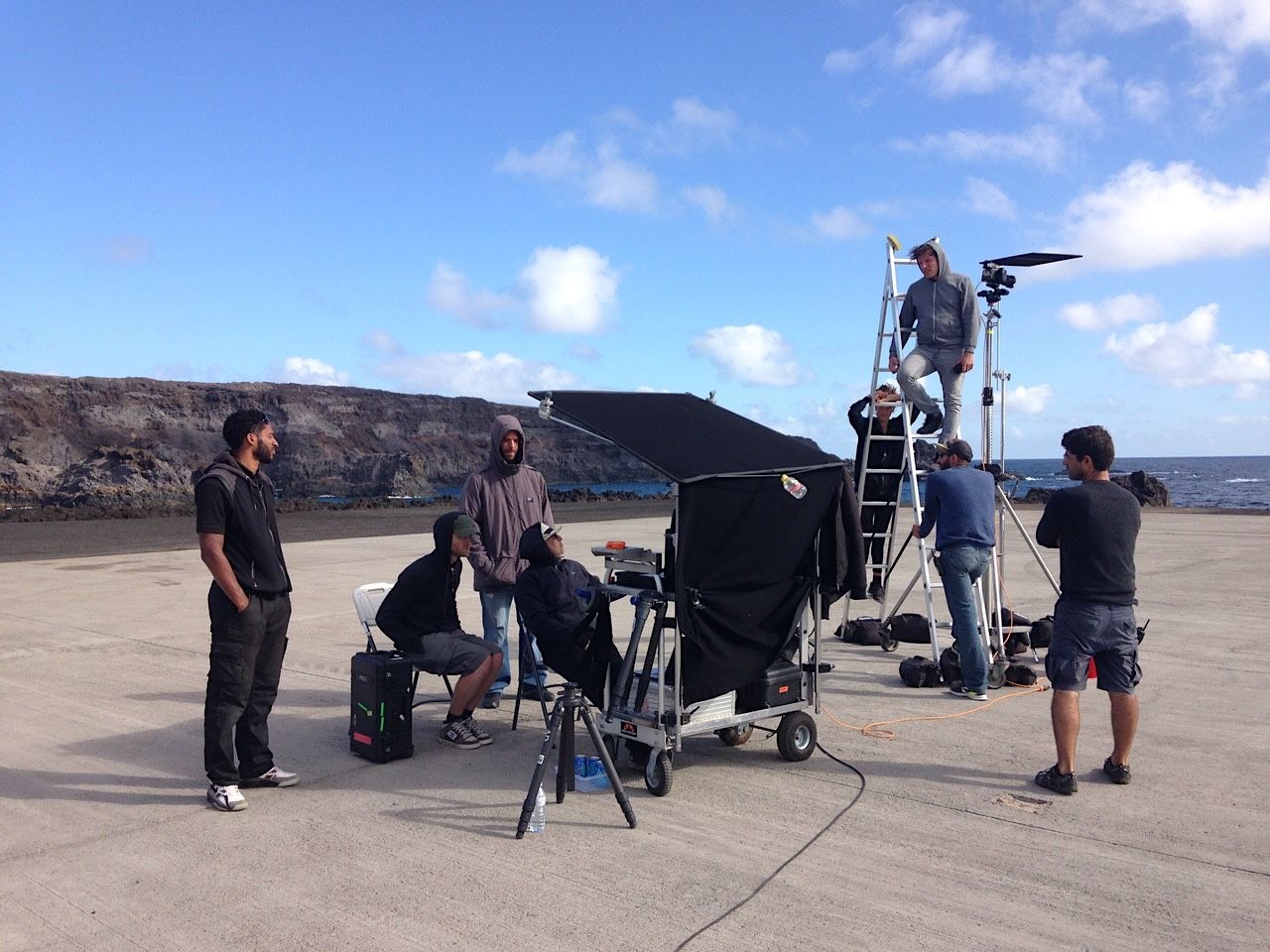 Film crew with camera, monitor and ladder on a volcanic coastline